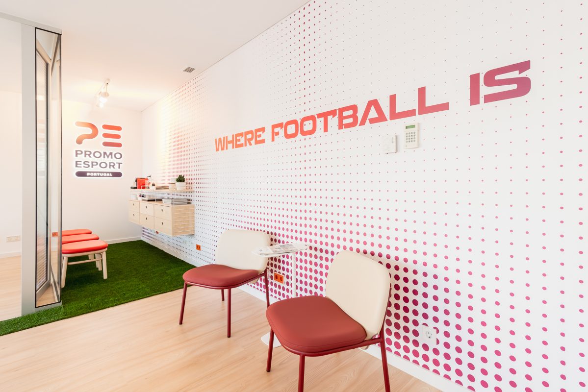 renovation of promoesport's offices in shades of white and red; white table and white chairs with plant and custom vinyl wall for the company