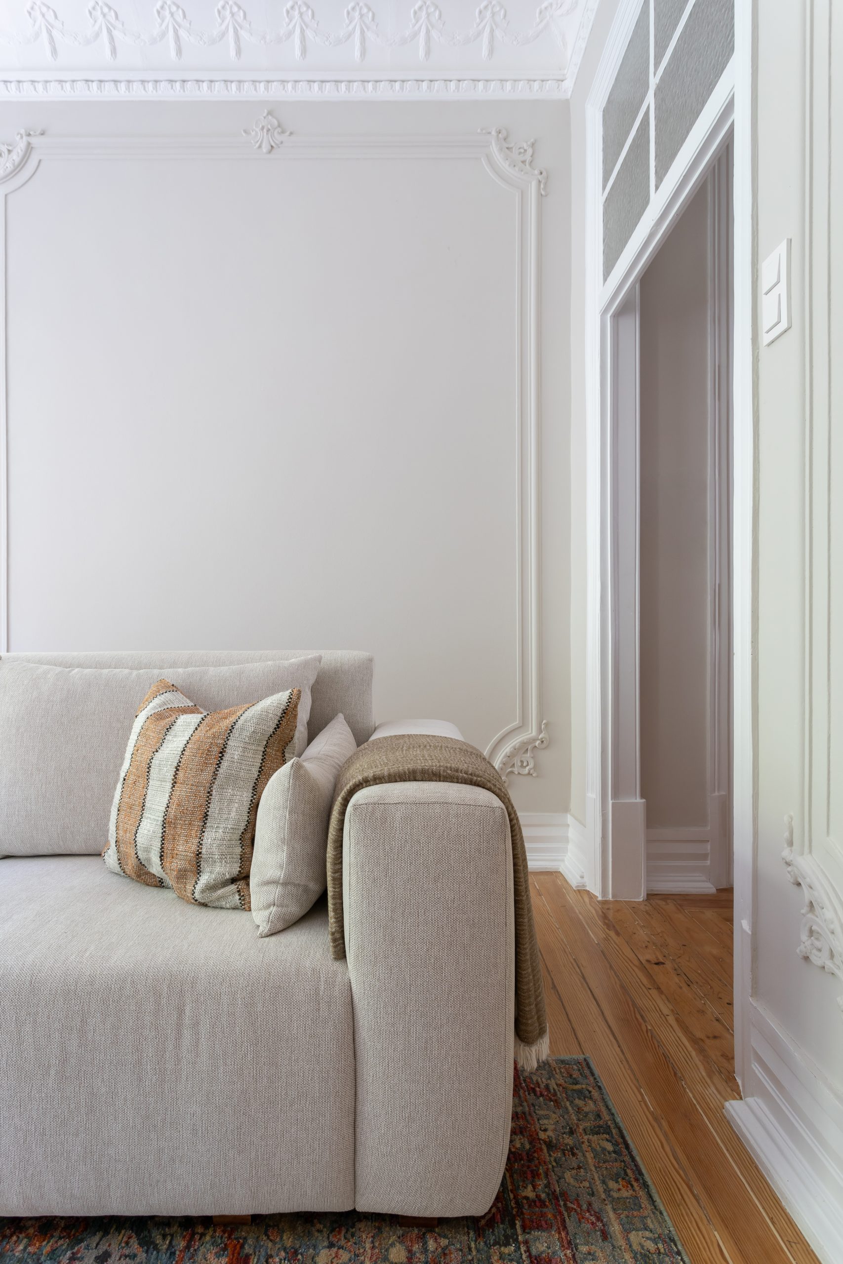 Renovação e Decoração da sala de estar da Casa das Avenidas; elementos arquitetónicos lisboetas originais com decoração intemporal e moderna; sofá moderno em tons claros com almofada Às riscas