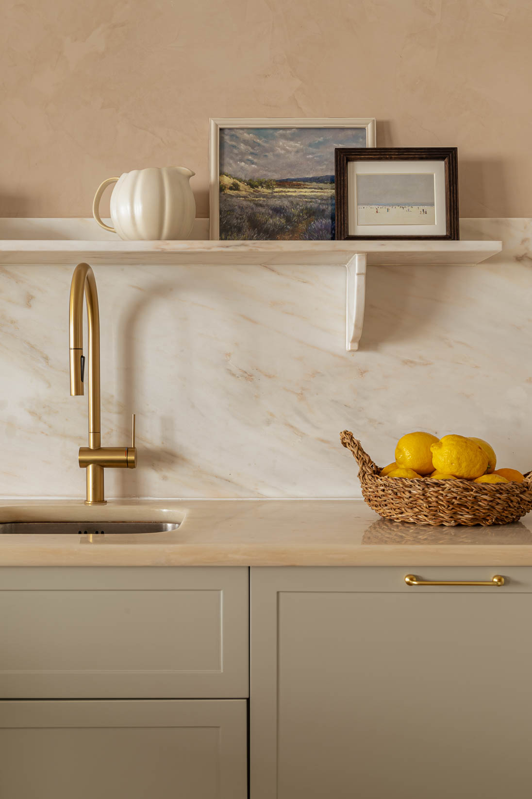 Casa do Paço - Cozinha aberta com banco de madeira, e bancada em mármore claro, móveis ripados a vere/sage green, com arrumação aberta. Backsplash a mármore branco; estante em mármore e hardware em metal dourado. Dispensa com porta de madeira e vidro