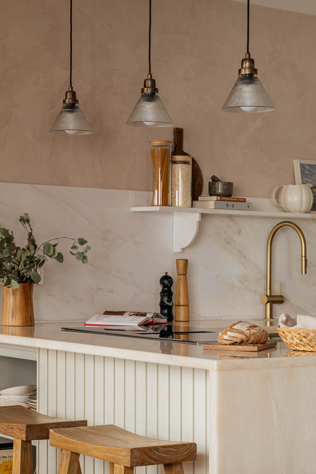 Casa do Paço - Cozinha aberta com banco de madeira, e bancada em mármore claro, móveis ripados a vere/sage green, com arrumação aberta. Backsplash a mármore branco; estante em mármore e hardware em metal dourado. Dispensa com porta de madeira e vidro